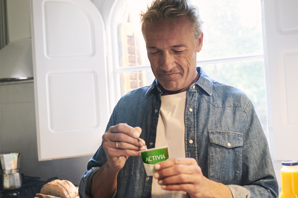 Man eating an Activia yoghurt in his kitchen