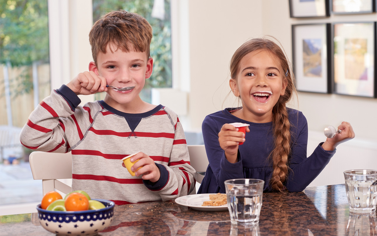 Deux enfants souriants en train de manger des yaourts Danonino en pots Deux enfants souriants en train de manger des yaourts Danonino en pots