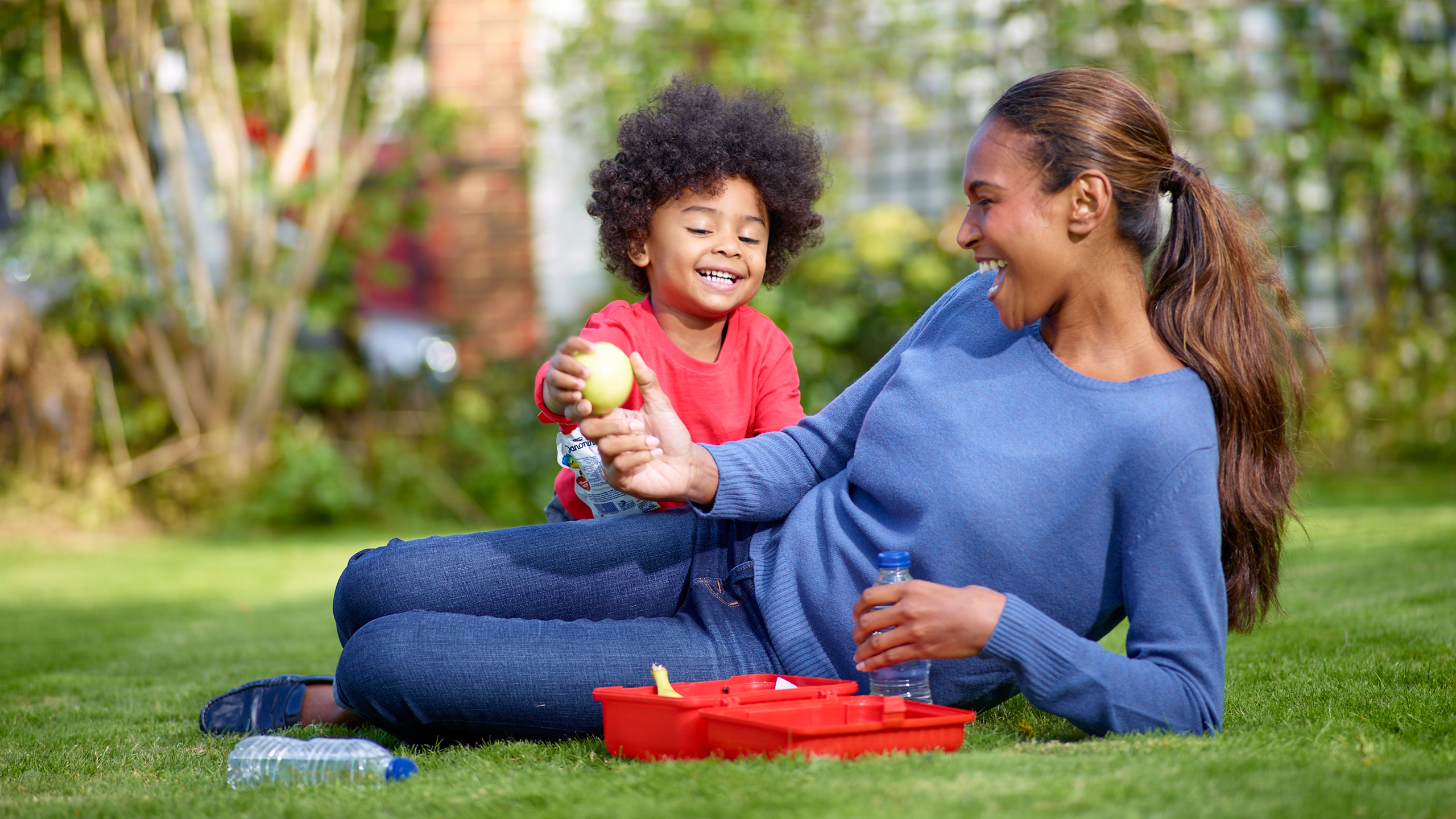 Une mère et sa fille allongées sur l'herbe, mangeant un produit Danonino