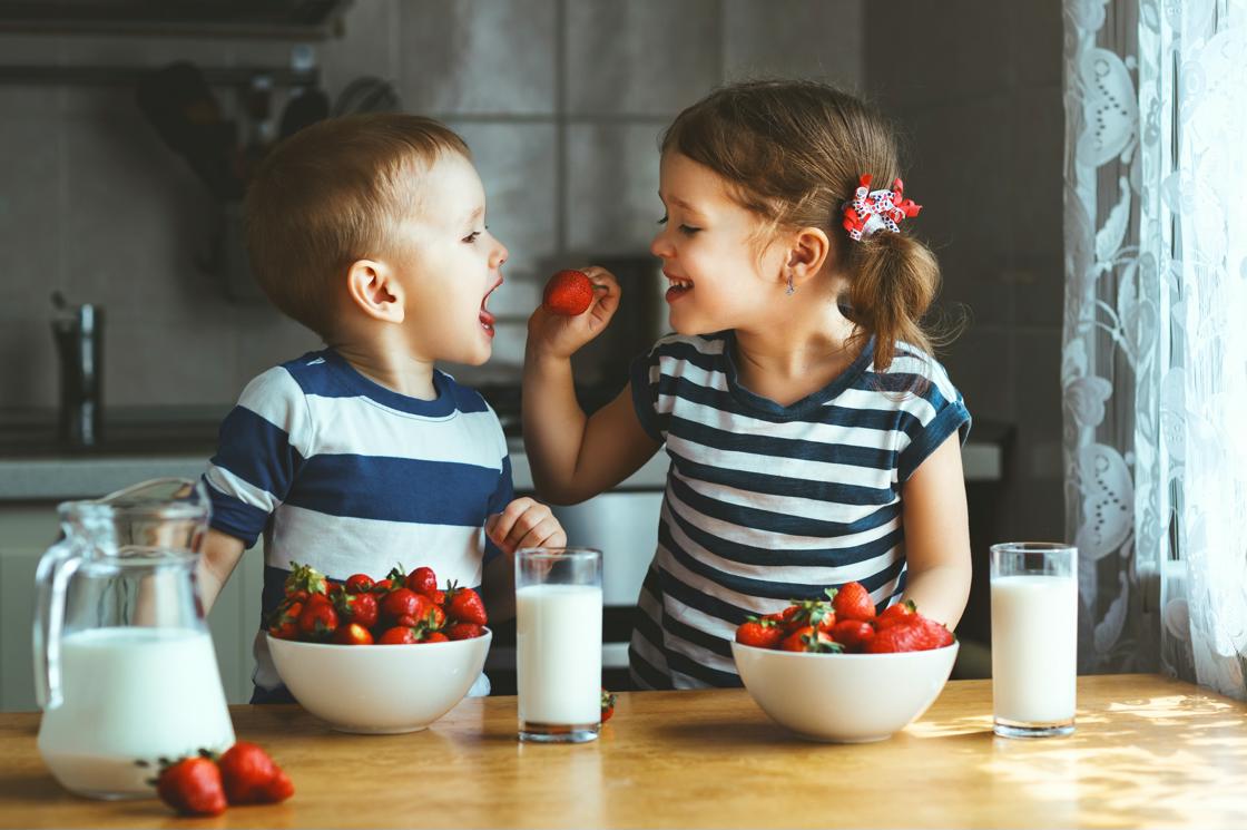 Deux enfants en train de manger des fraises avec un verre de lait Deux enfants en train de manger des fraises avec un verre de lait