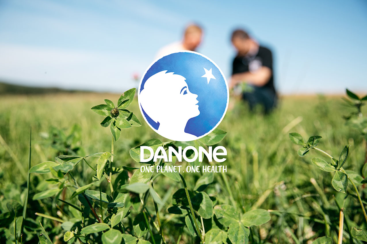 Danone - One planet. One health. Logo devant un champ et deux agriculteurs au second plan